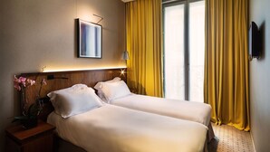 A hotel room with two beds, a TV, a framed picture, and a window with yellow curtains. - Hotel Chateaudun Opera (Paris)