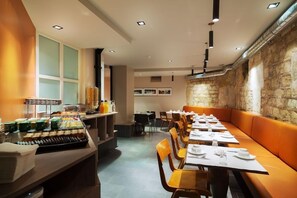 A restaurant with a long counter, orange seating, and a stone wall. - Hotel Chateaudun Opera (Paris)