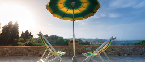 A patio with two lounge chairs and a large umbrella, overlooking a scenic landscape.