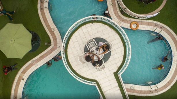 Vista aérea de una zona de piscina con múltiples piscinas interconectadas, una fuente central y paseos alrededor.