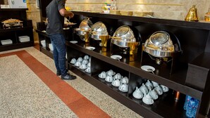 Zona de bufé con múltiples estaciones de servicio, que incluyen opciones de comida caliente y fría, además de una variedad de cubiertos y platos.