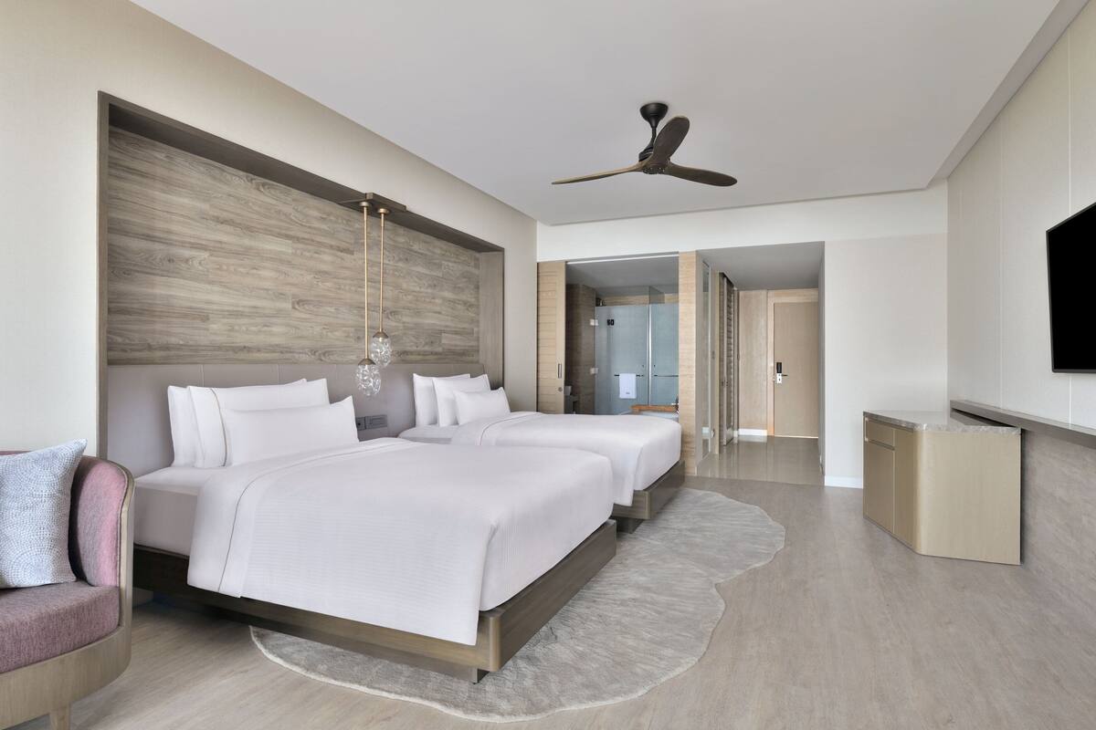 A modern hotel room with a large bed, a ceiling fan, a TV, and a walk-in closet.