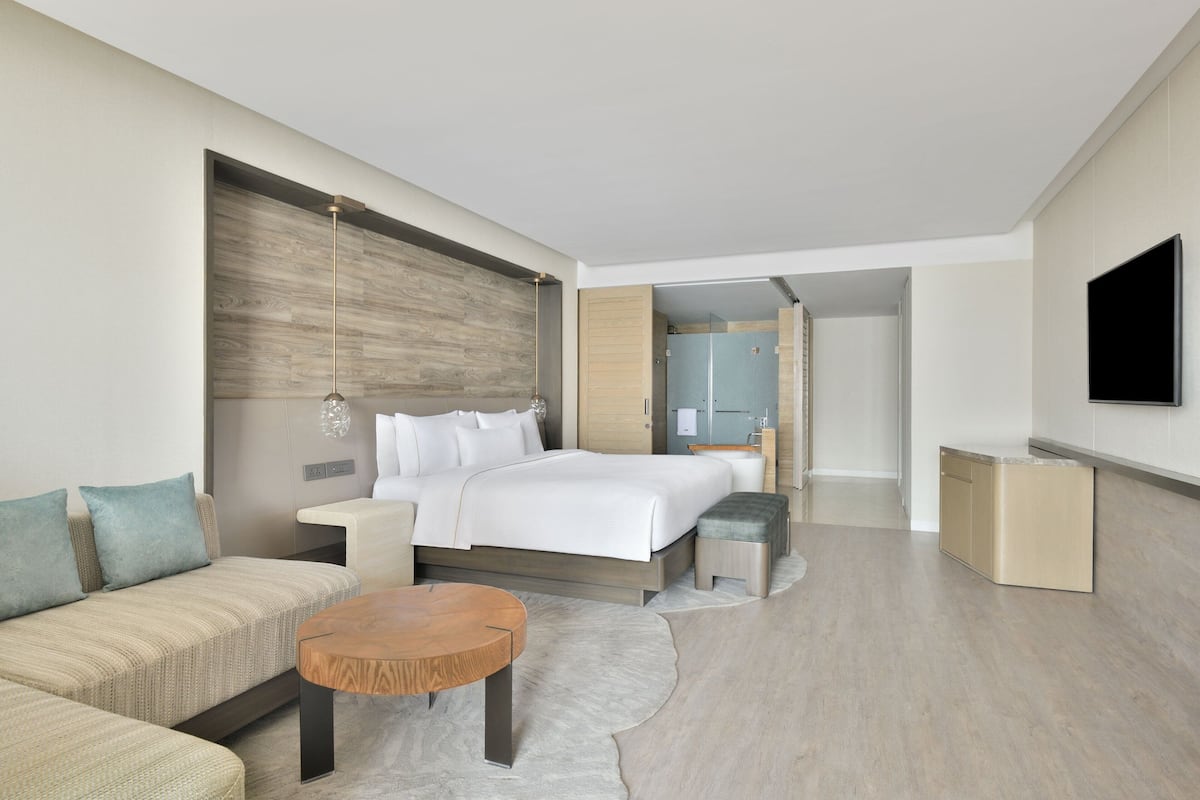 A modern hotel room with a large bed, a sofa, a coffee table, and a TV.