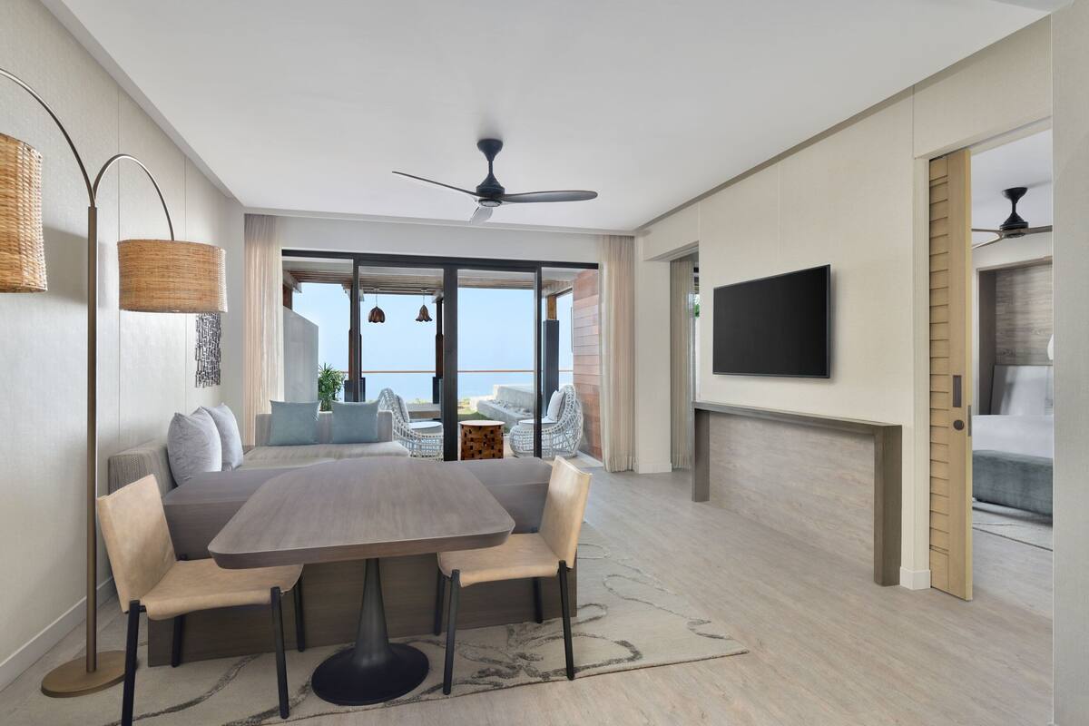 A modern living room with a dining area, a ceiling fan, a flat-screen TV, and a view to the outside.