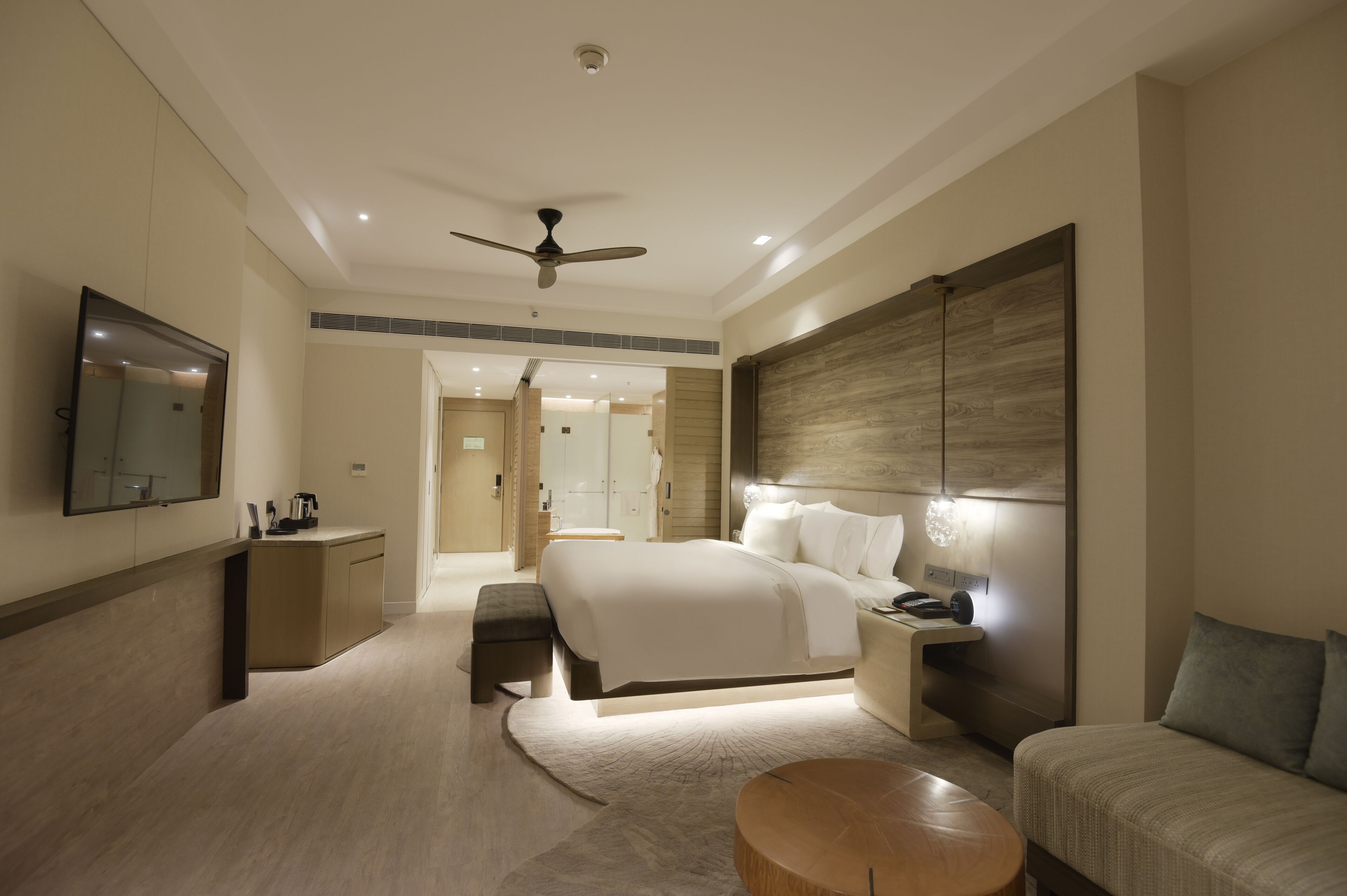 A modern hotel room with a large bed, a desk, a sofa, a ceiling fan, and a large mirror.