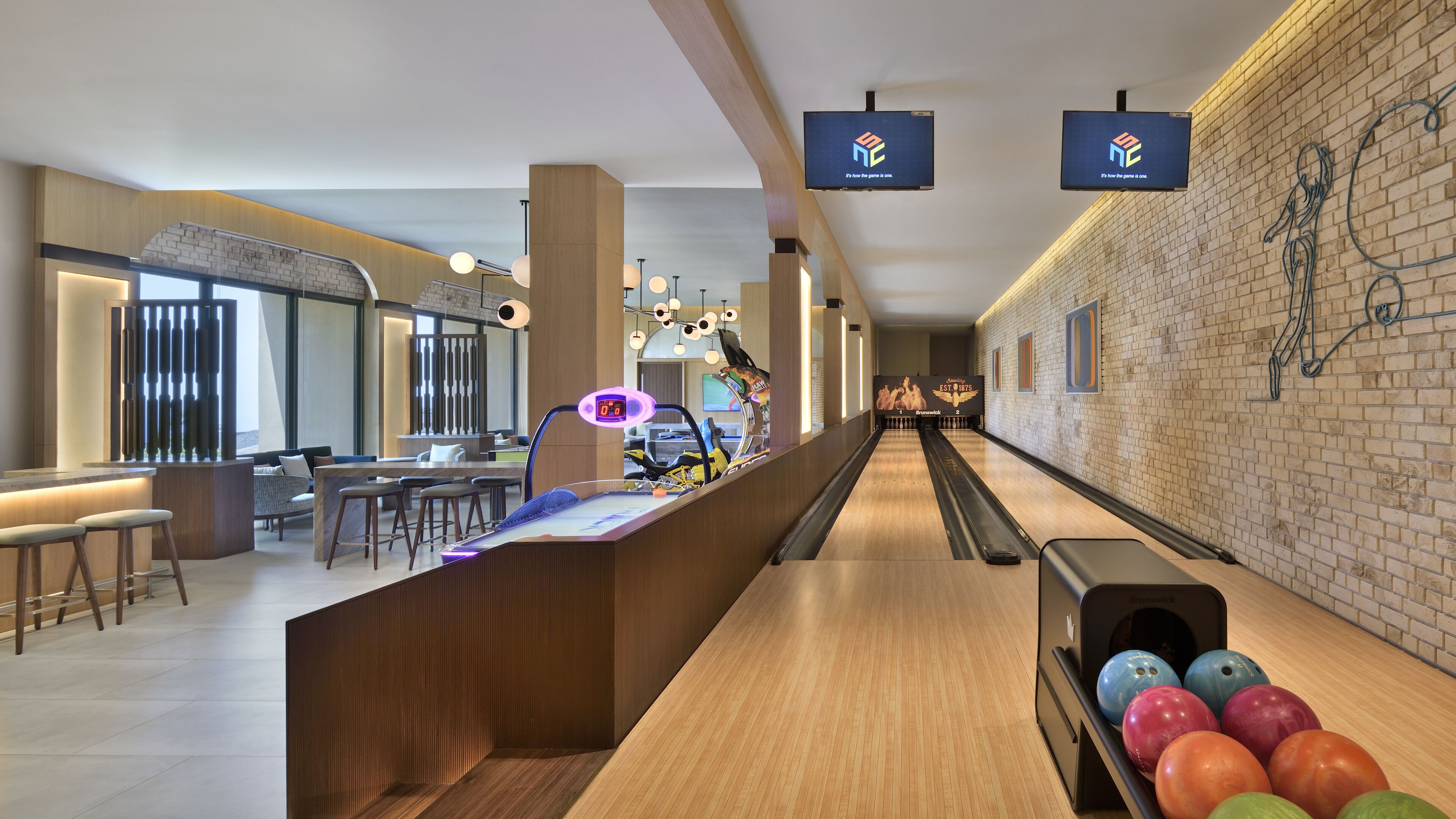 A bowling alley with a wooden floor, a counter with stools, and a bowling ball rack.