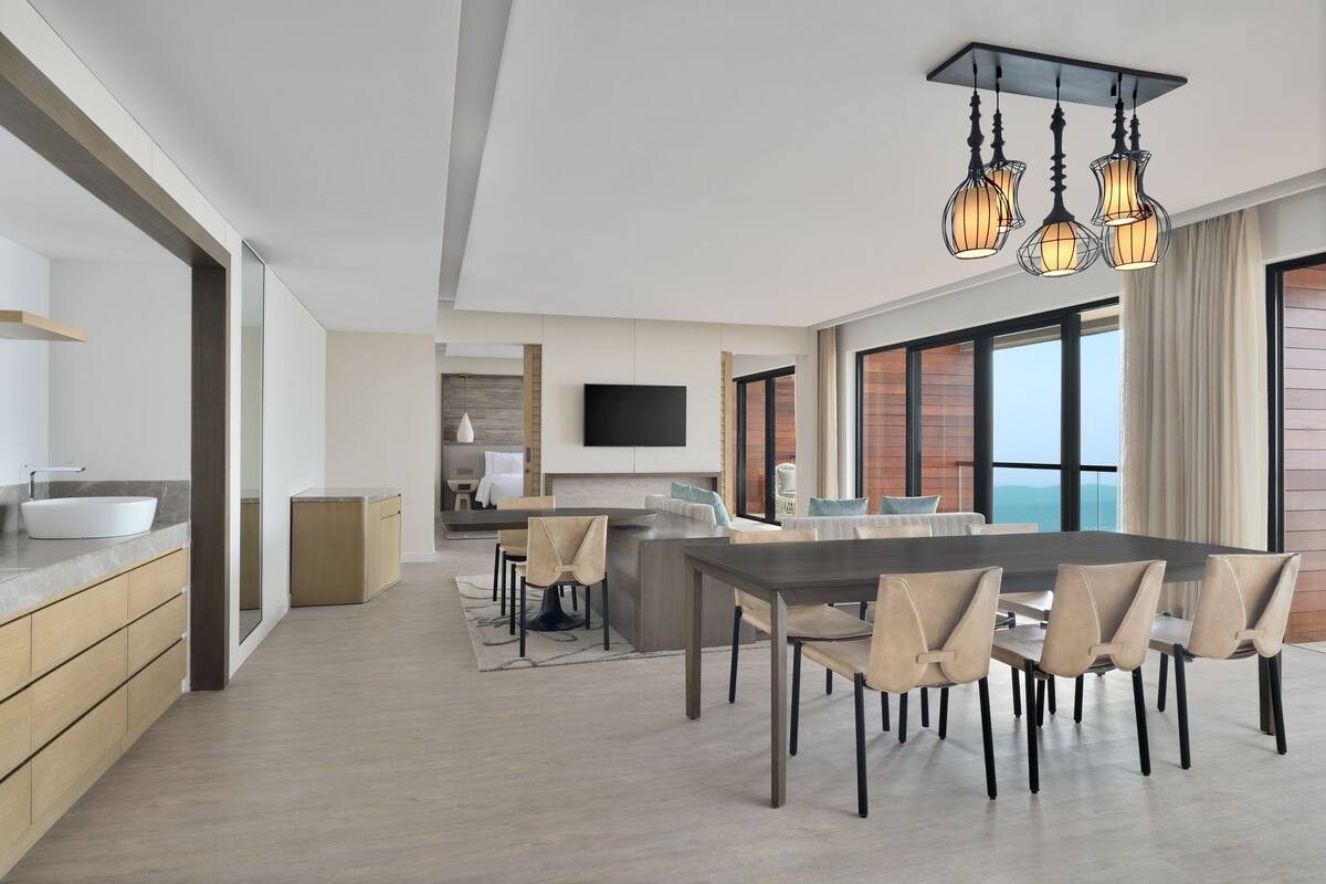 A modern kitchen with a large island, a dining area with a long table and chairs, and a large window offering a view.