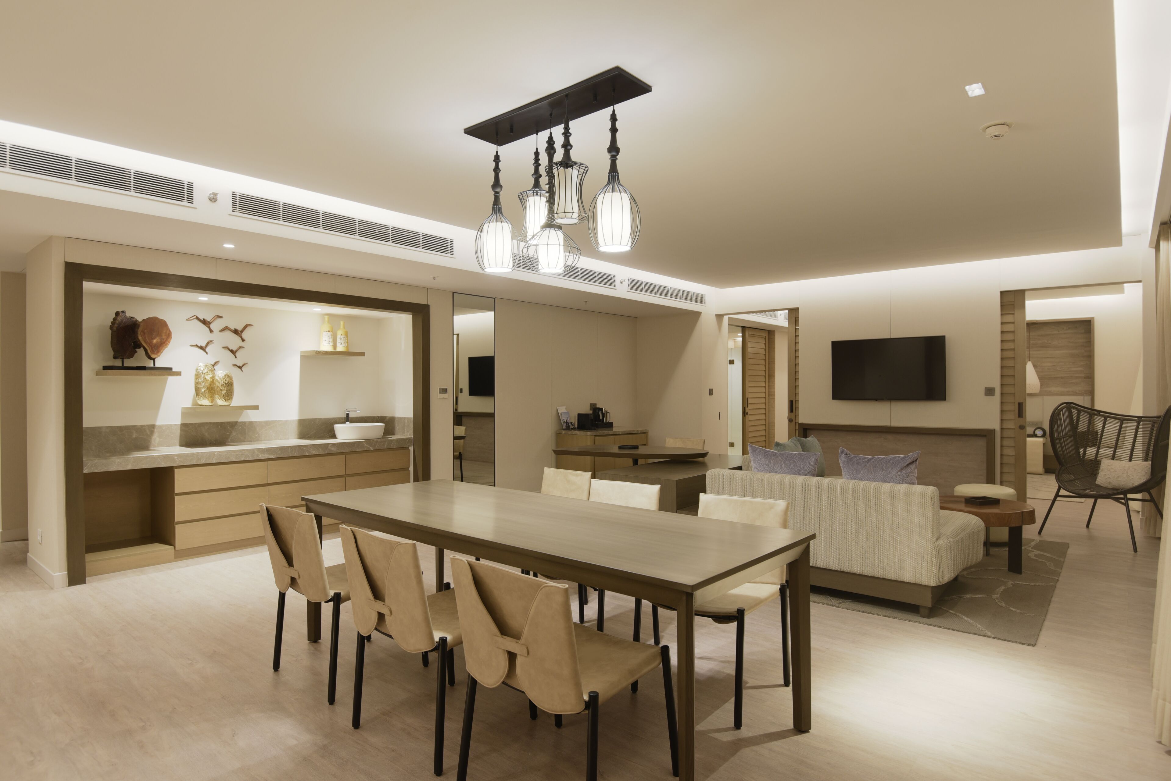 A modern kitchen with a central island, a dining area with a long table and chairs, and a living area with a sofa and a TV.