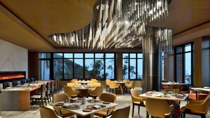 Un comedor moderno con mesas y sillas, ventanas amplias que ofrecen vistas al exterior y una lámpara original.