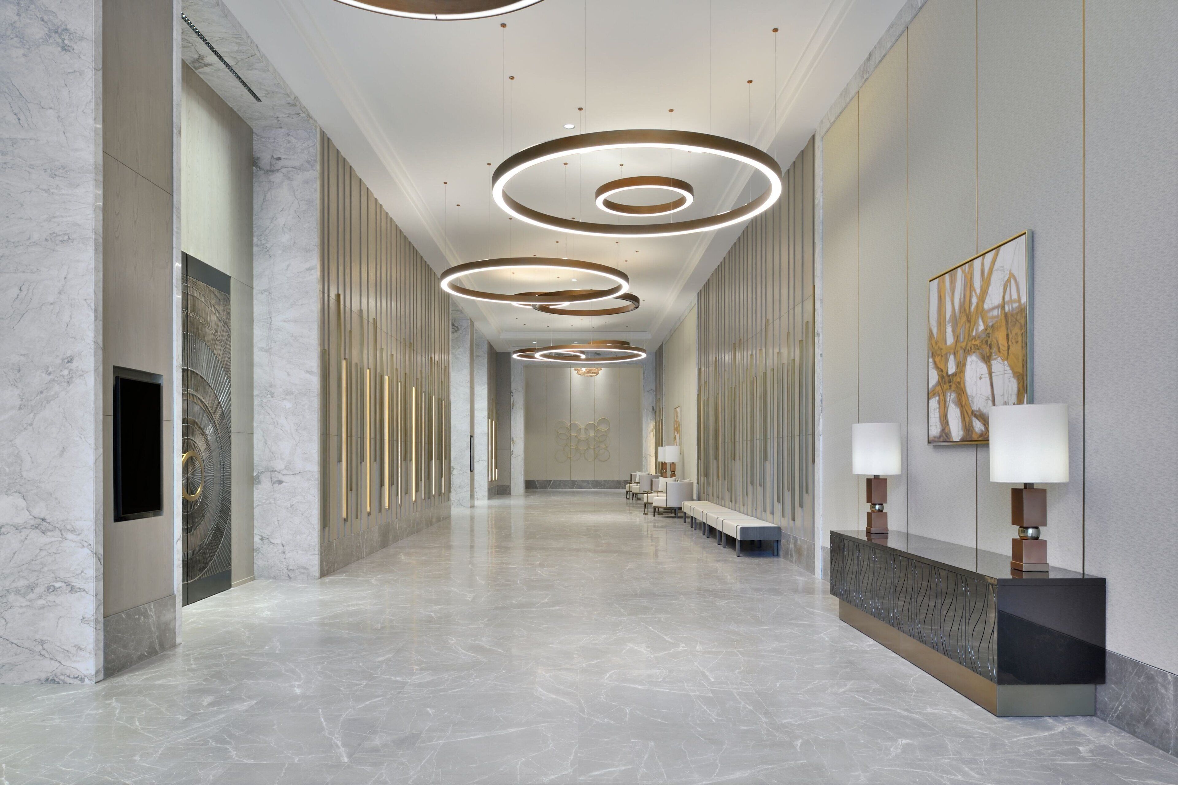 A modern hotel lobby with a marble floor, circular ceiling lights, and a reception desk with lamps.
