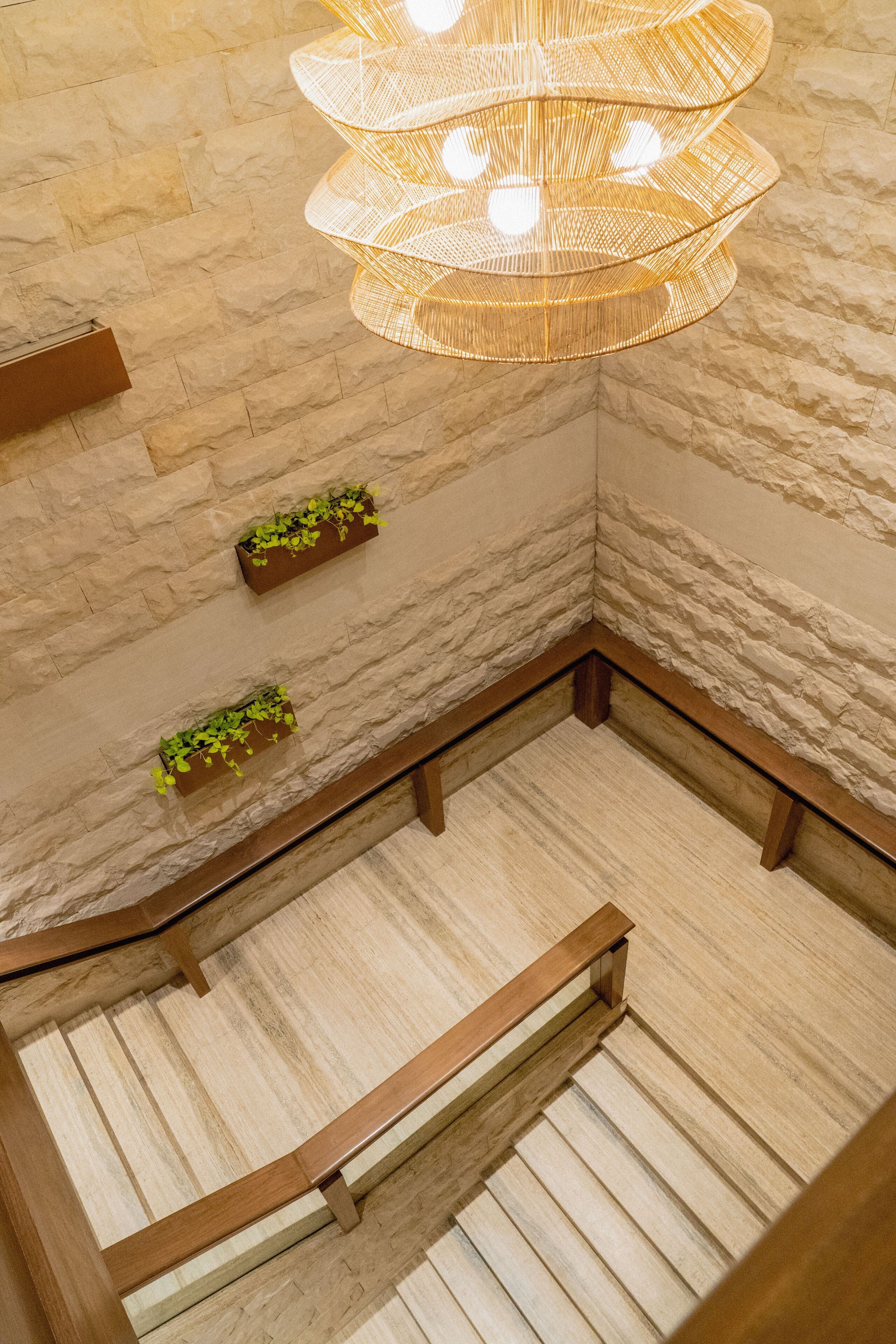 Un escalier avec des rampes en bois, un mur en pierre et un luminaire suspendu.