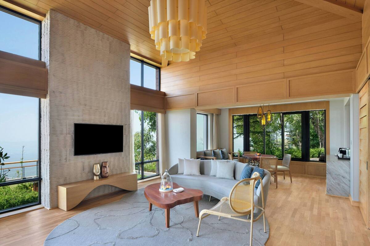A spacious living area with a large window, a flat-screen TV, a wooden ceiling, and a cozy seating arrangement.