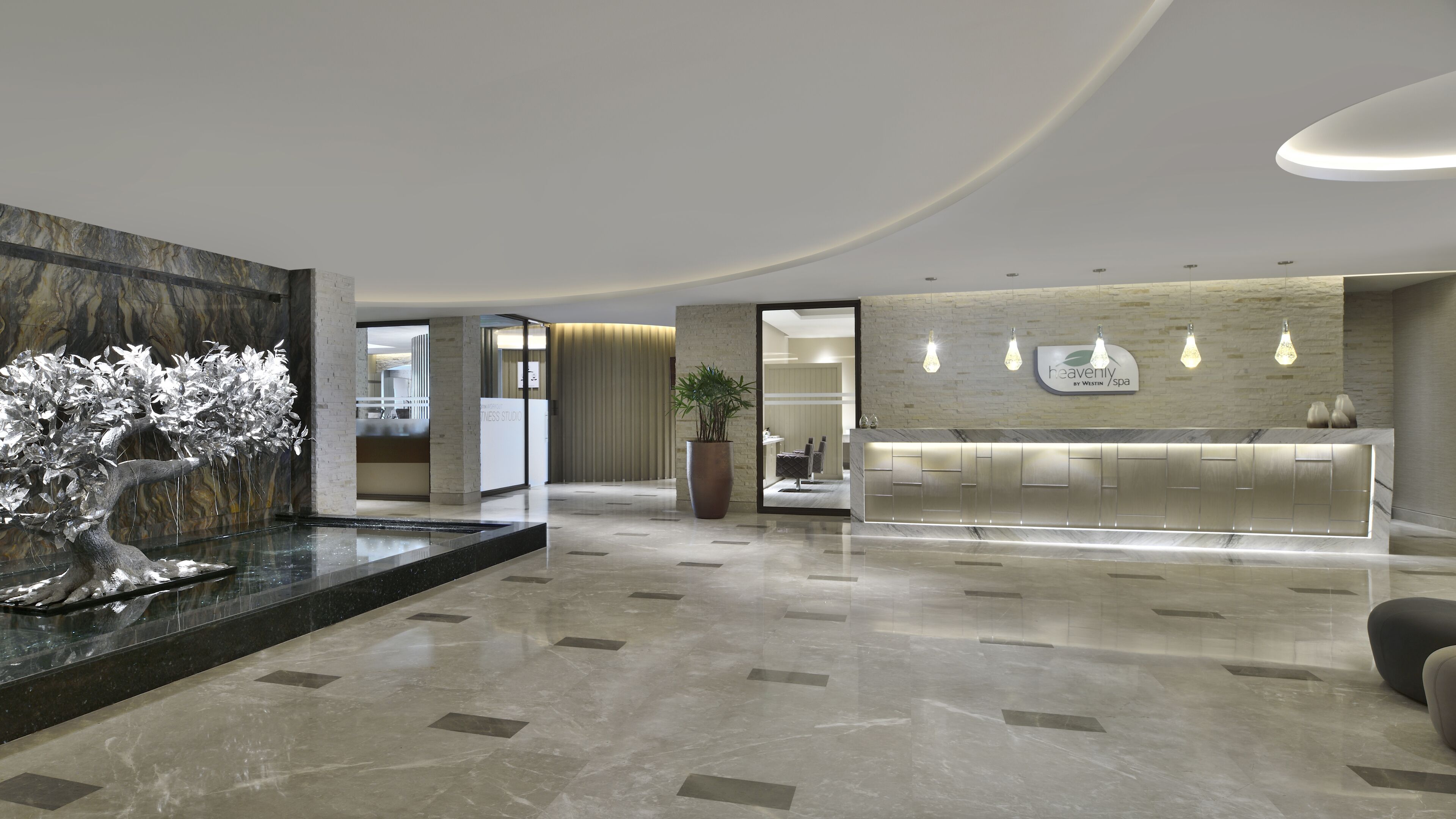 A modern lobby with a reception desk, a decorative tree sculpture, and a large potted plant.