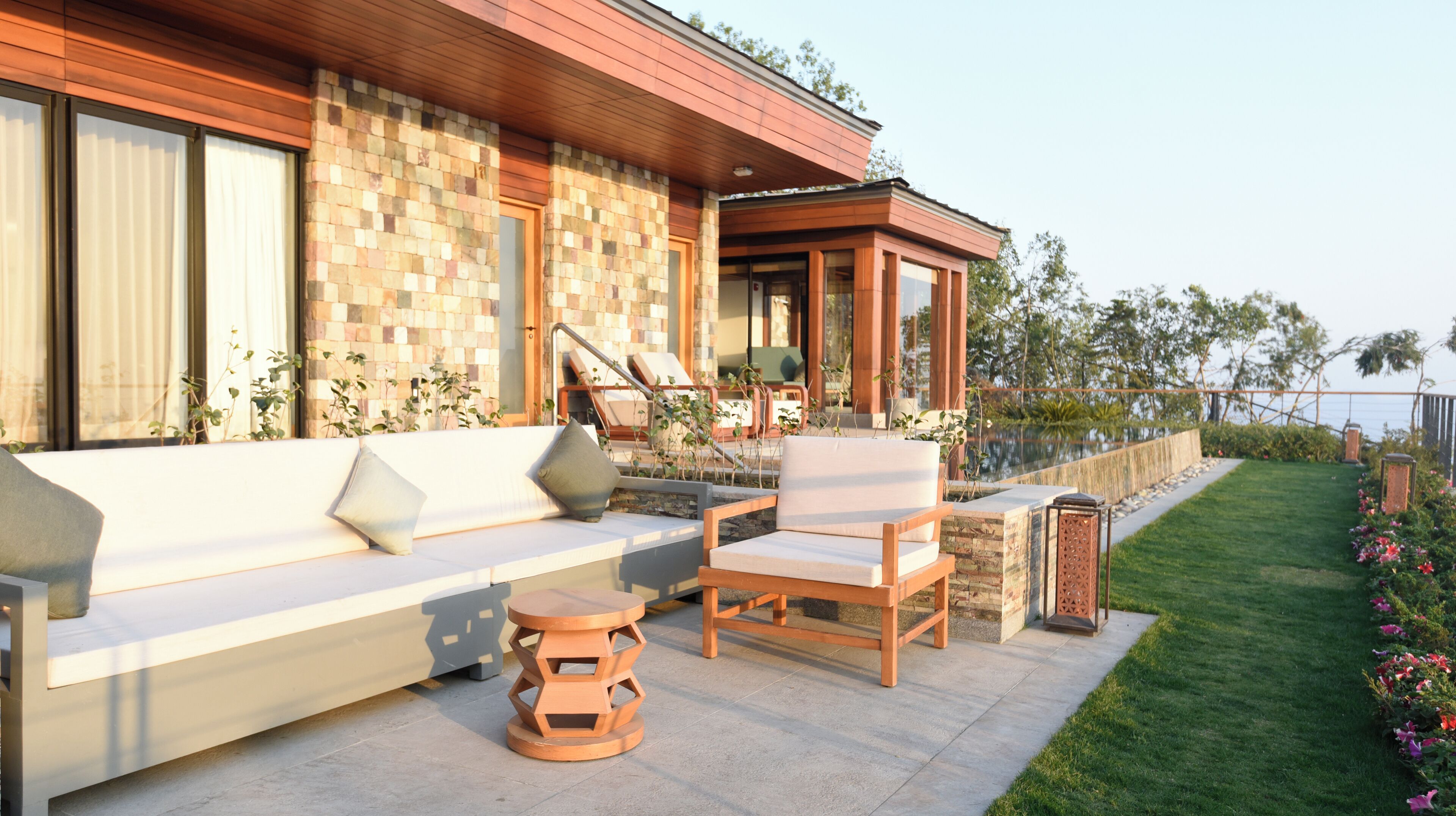 A modern outdoor seating area with a stone wall, a wooden deck, and a view of the ocean.