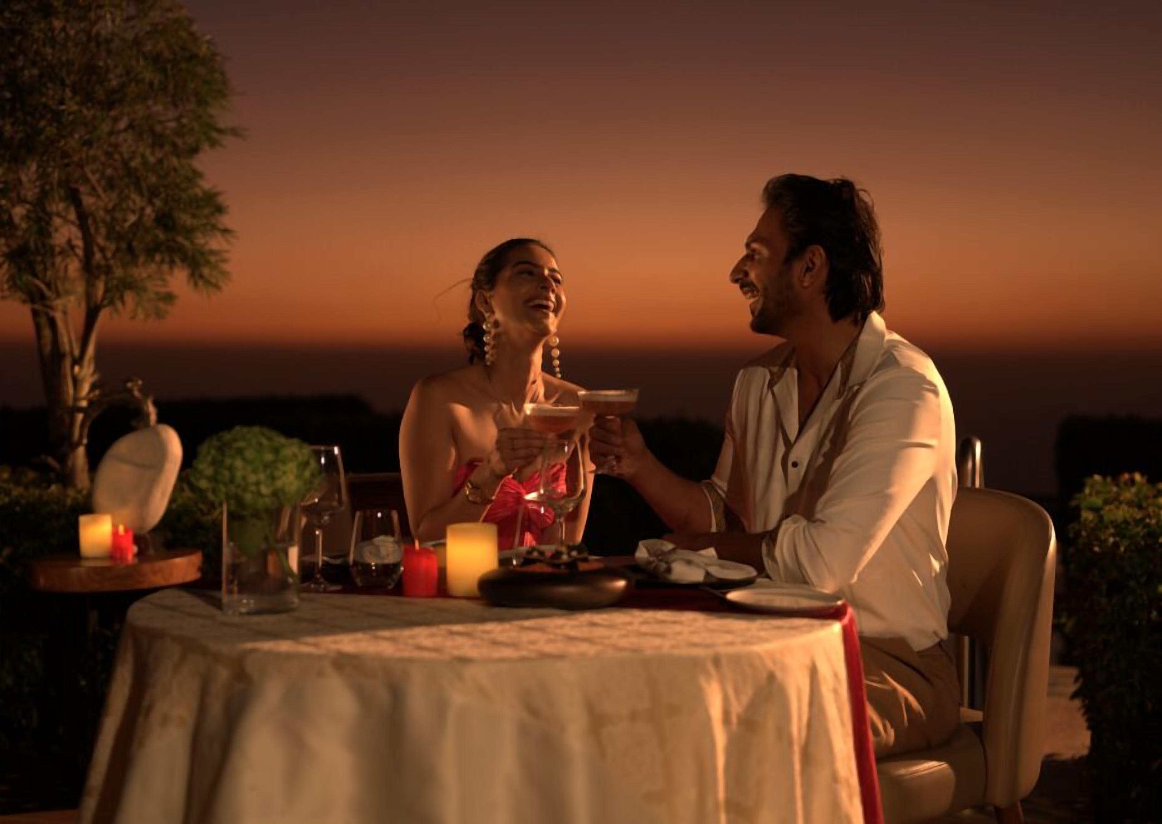 A couple dining at an outdoor table with candles and a view of the sunset.