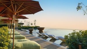 Zona junto a la piscina con sillones reclinables y sombrillas, cielo despejado y vista al agua.