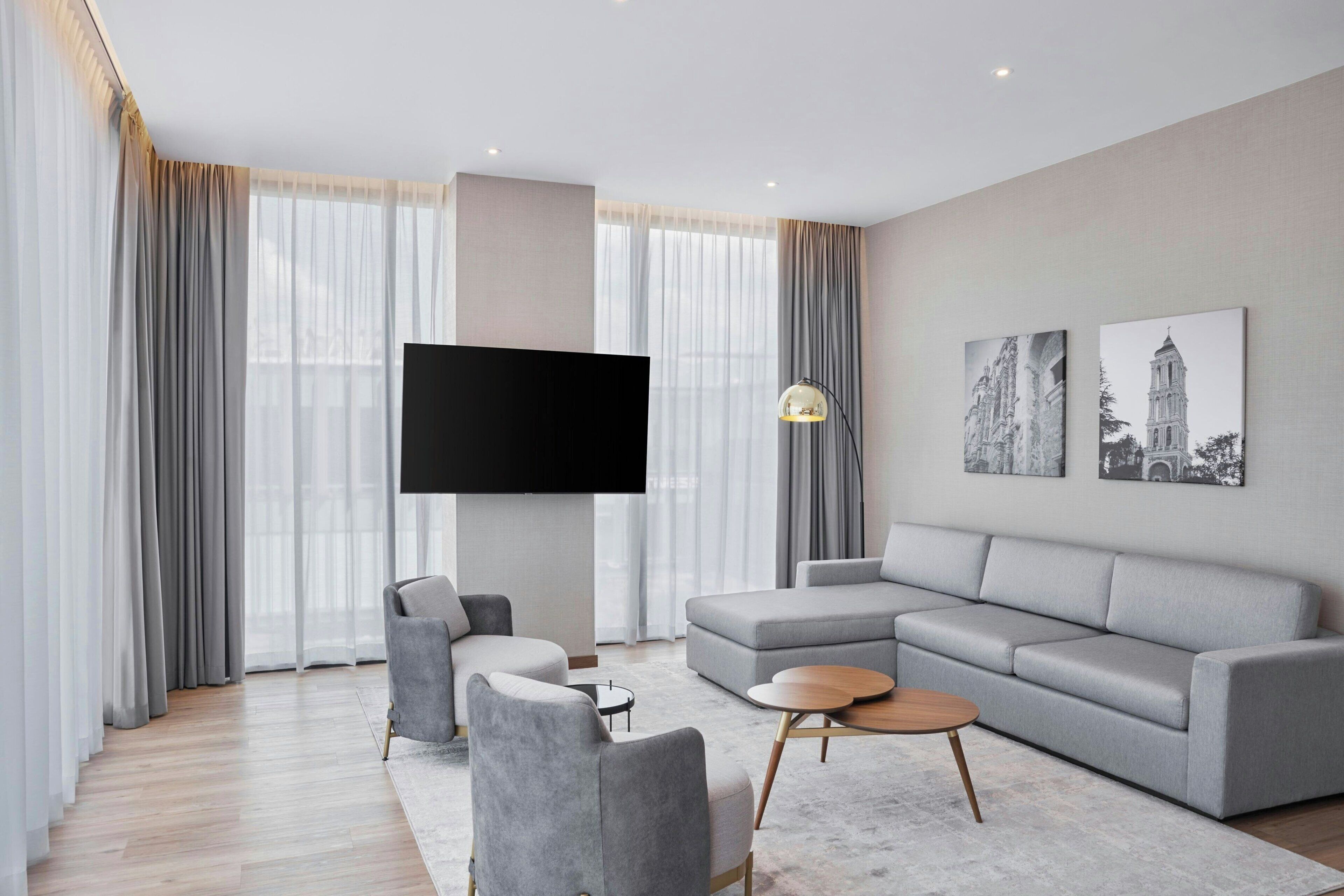Una sala de estar moderna con un sofá seccional gris, un sillón gris, una mesita de centro redonda y un televisor de pantalla plana montado en la pared.