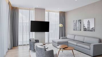 Una sala de estar moderna con un sofá seccional gris, un sillón gris, una mesita de centro redonda y un televisor de pantalla plana montado en la pared.