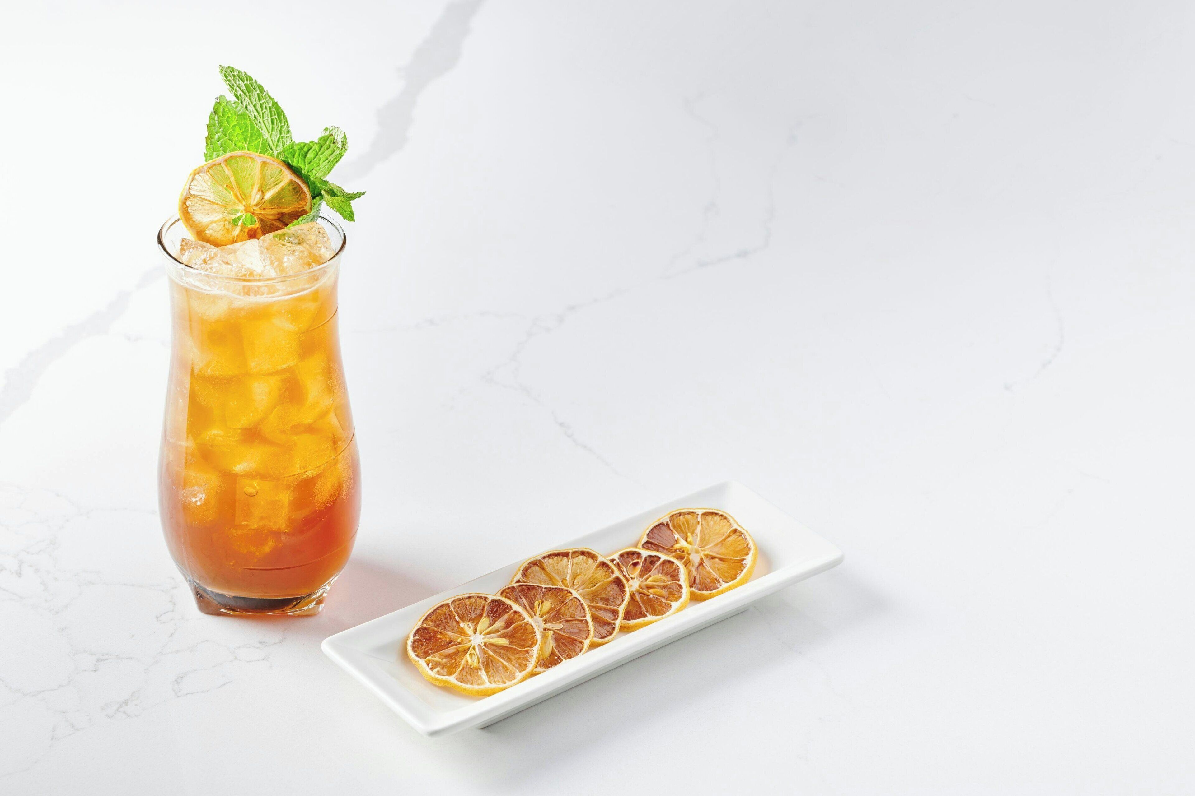 A glass of iced tea with a lime slice and mint garnish, accompanied by a white plate with dried orange slices.