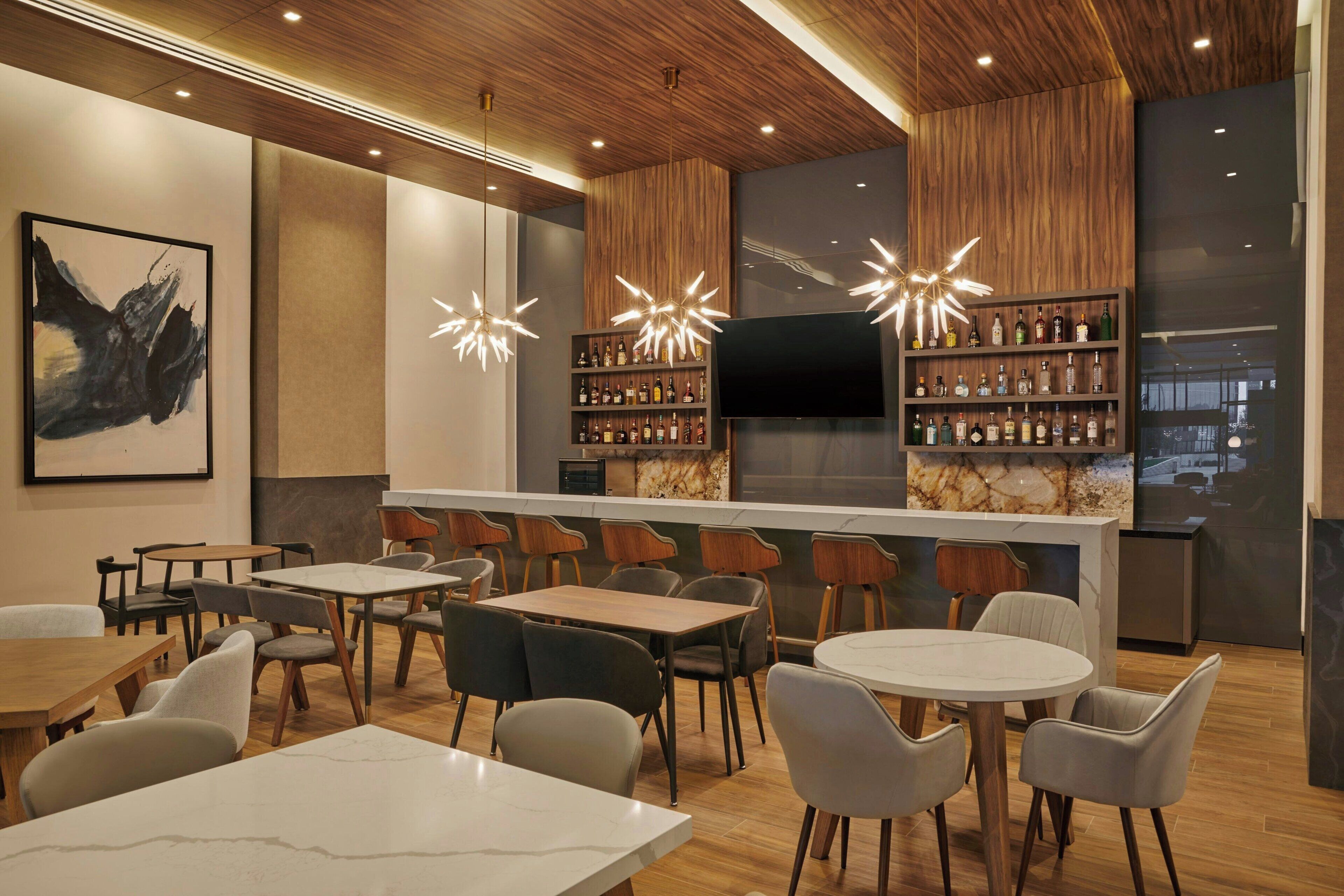 A modern bar area with wooden ceiling, bar stools, and a variety of liquor bottles.