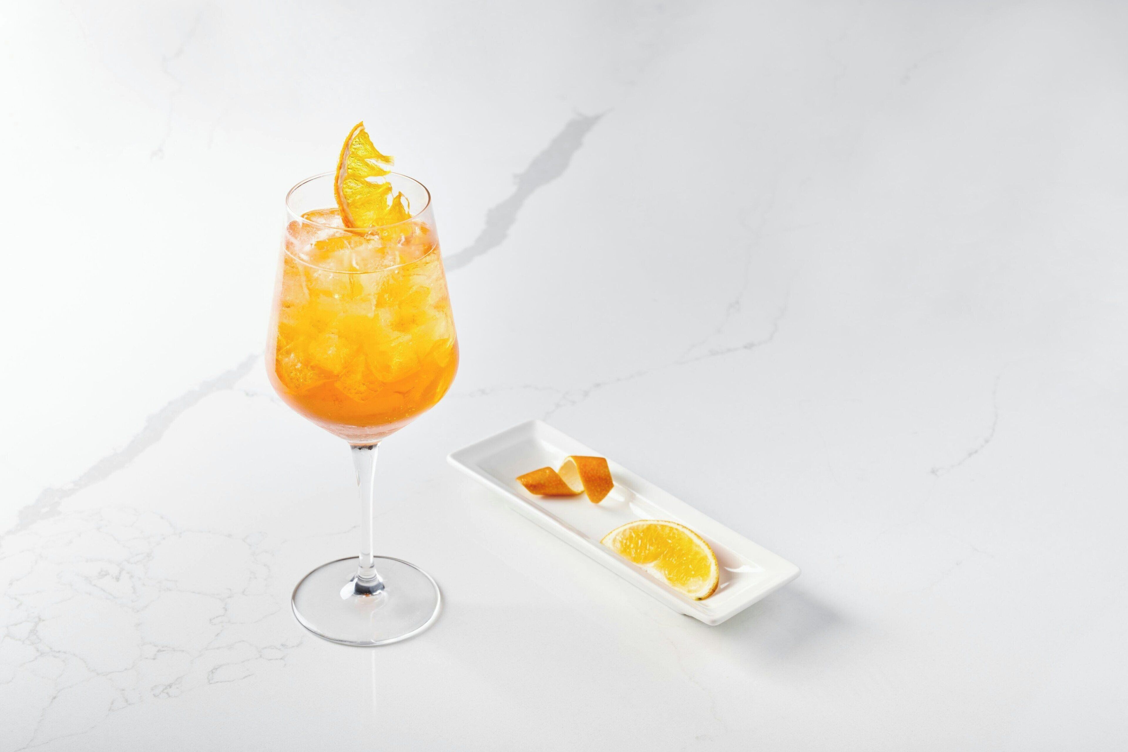 Un vaso de jugo de naranja con una rodaja de naranja en el borde, sobre una superficie de mármol blanco.