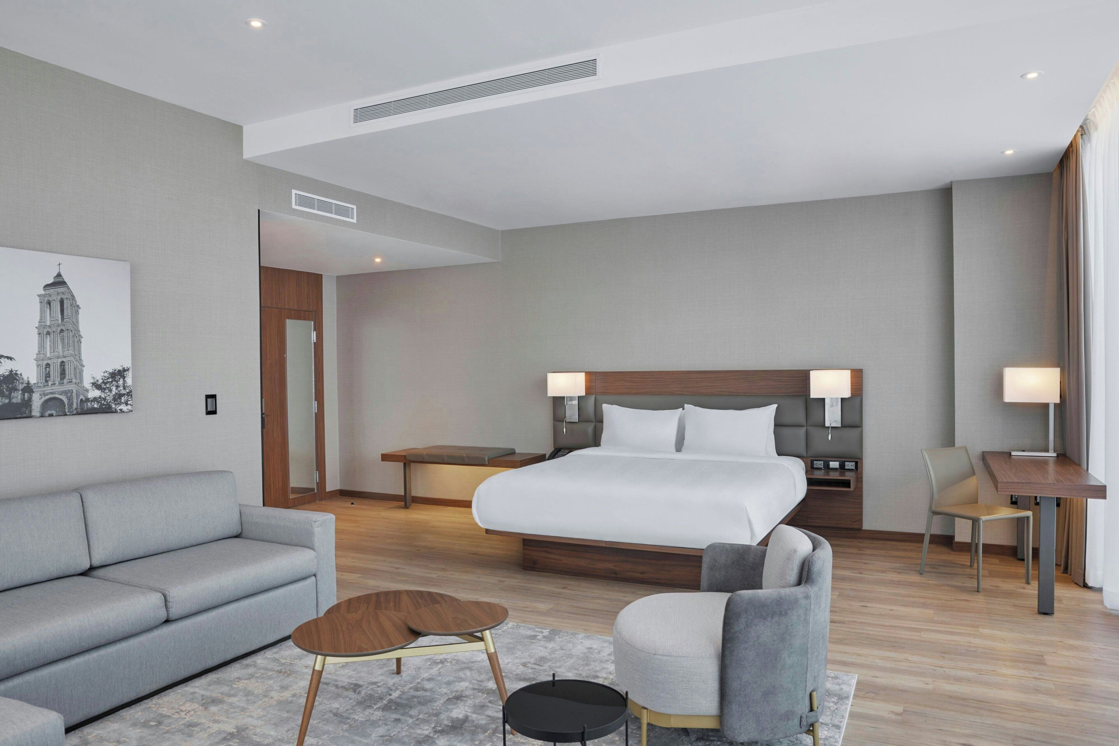 Una habitación de hotel moderna con una cama grande, un sofá, una mesita y una silla.