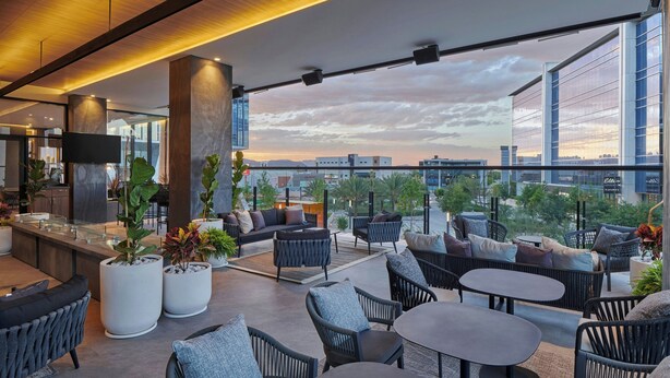 A modern rooftop lounge with outdoor seating, a bar area, and a city view.