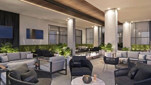 A modern outdoor lounge area with sofas, chairs, and tables, surrounded by large windows and plants.
