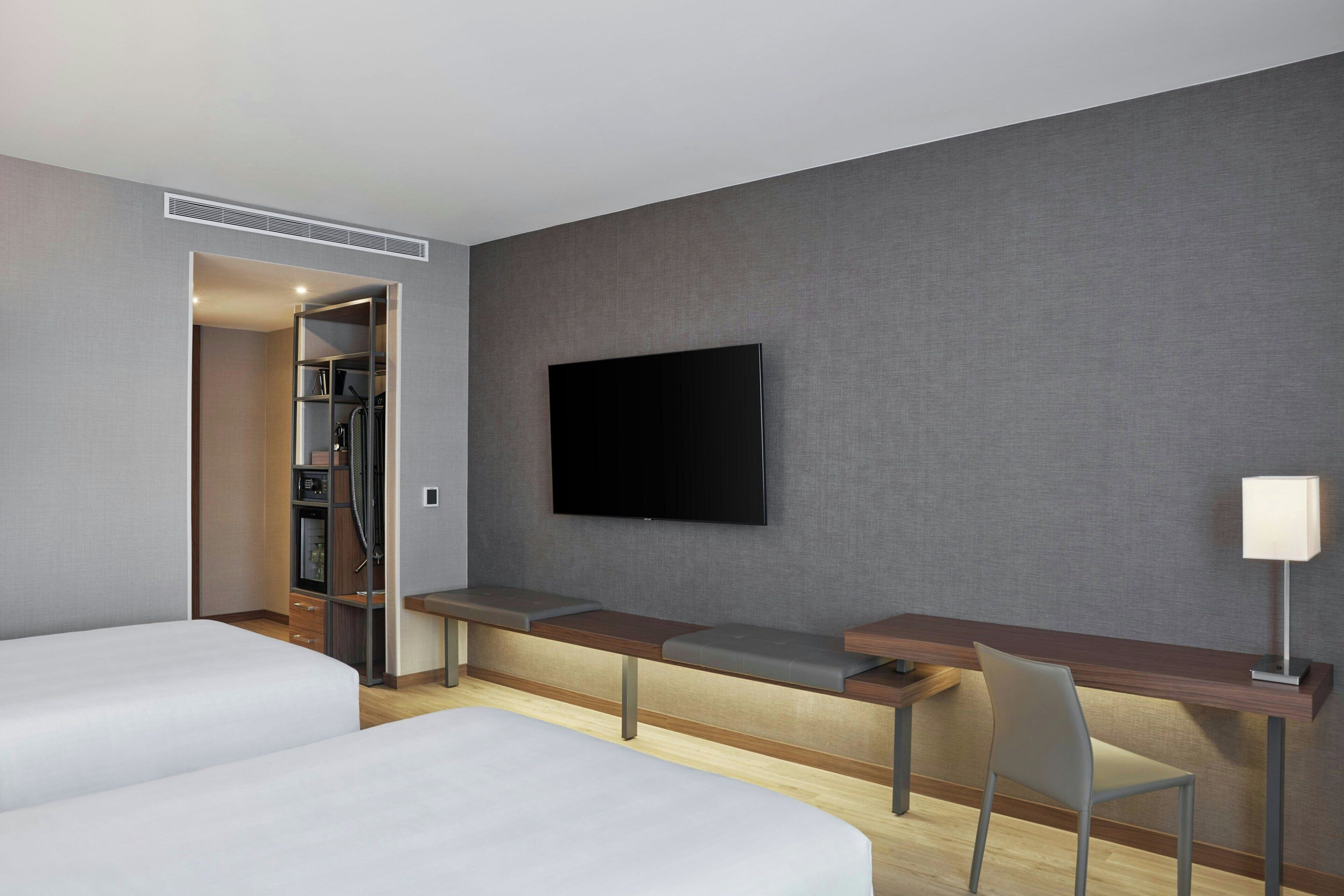 A hotel room with two beds, a desk with a chair, a TV mounted on the wall, and a closet.