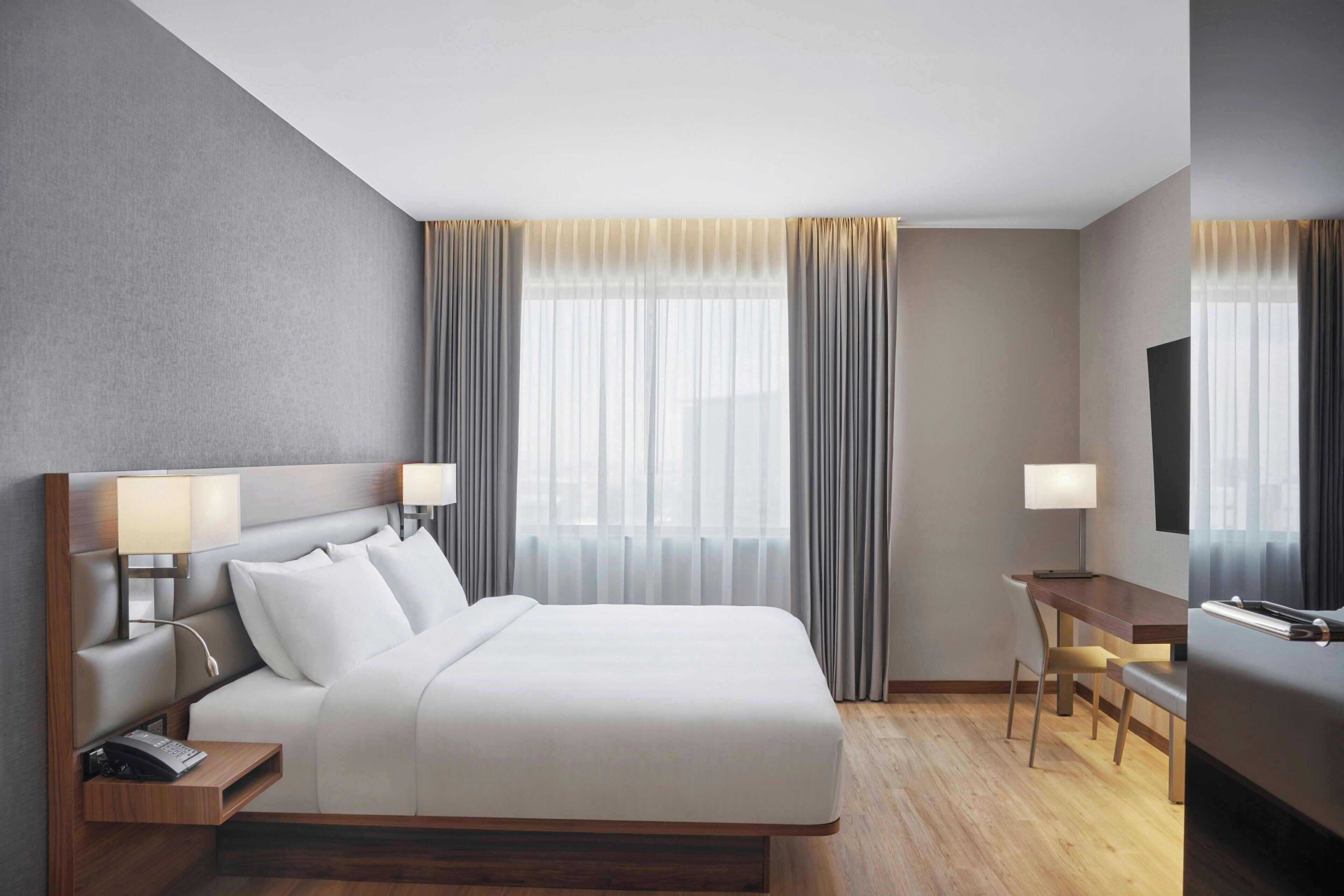 A modern hotel room with a large bed, bedside lamps, a desk, and a TV.