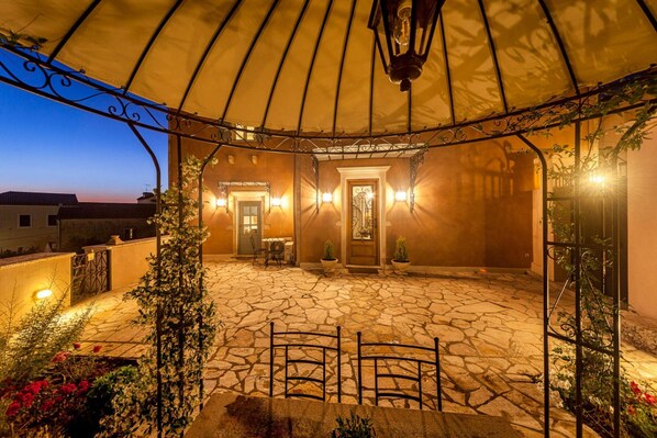 An outdoor patio with stone flooring, metal chairs, and a canopy.