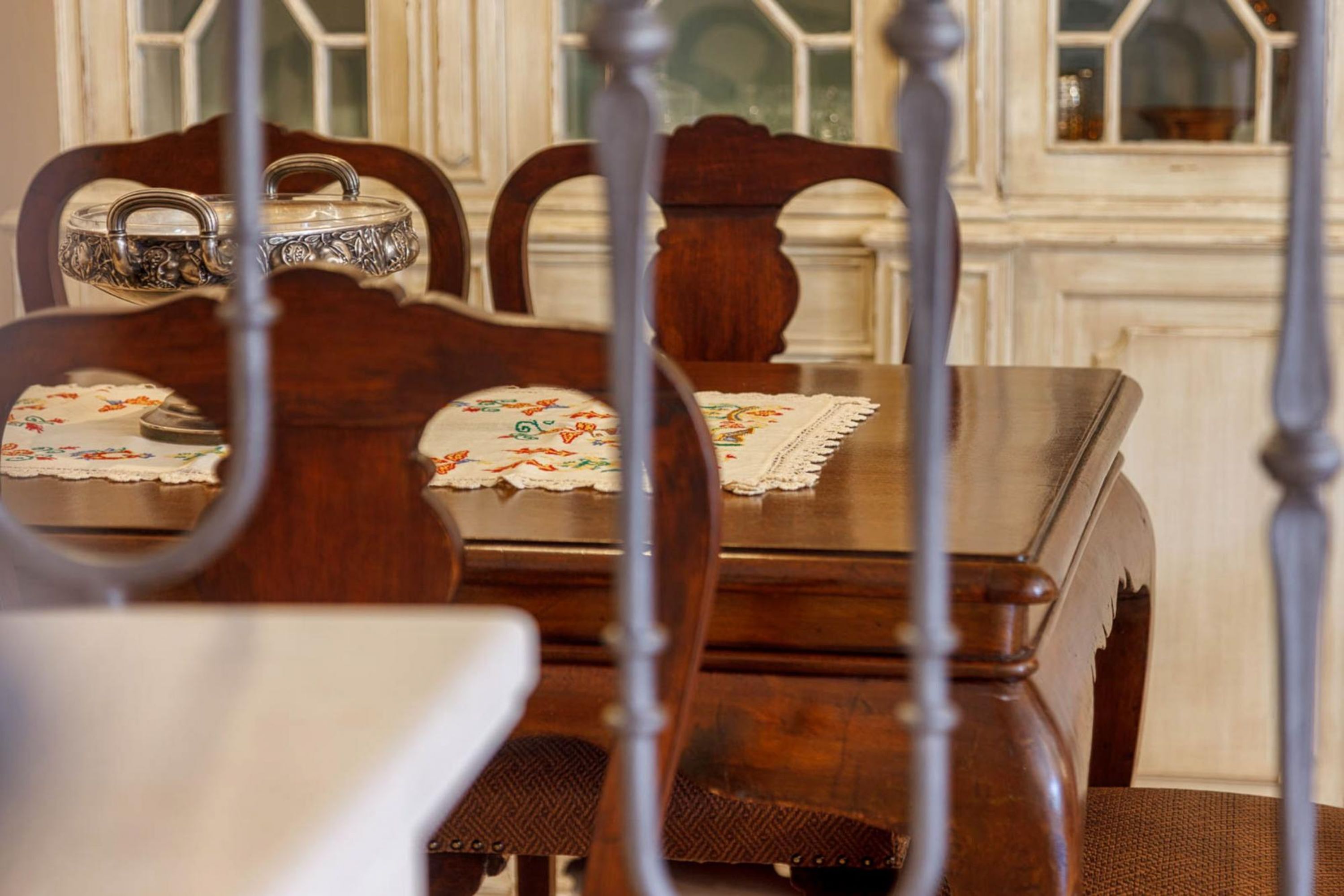 Een eettafel met een tafelkleed met bloemenprint, omringd door houten stoelen met een decoratief metalen bovenblad.