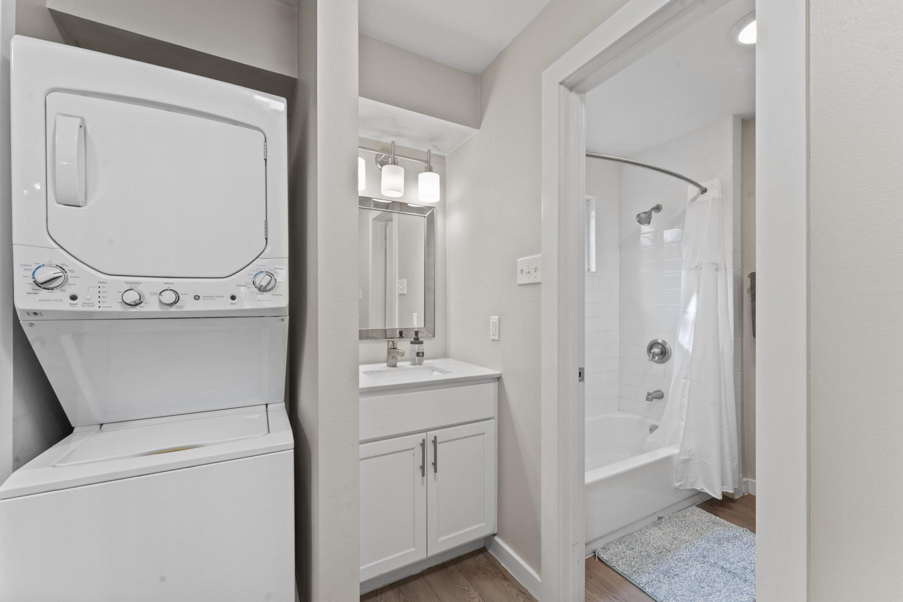 Een moderne badkamer met een ingebouwde wasmachine en droger, een wastafel met spiegel en een inloopdouche.