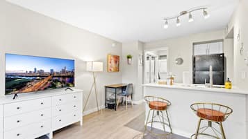 Een moderne keuken met een grote koelkast, een eethoek met twee barkrukken, een tv bevestigd aan een kast, en een stadsgezicht op de muur.