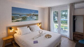 Habitación de hotel con cama, un cuadro, mesita de noche, televisor y puerta corrediza de vidrio a un área exterior.