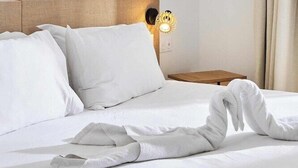 Una habitación de hotel con una cama, almohadas blancas, un cuadro de un pájaro en la pared y una mesita de noche con una lámpara.
