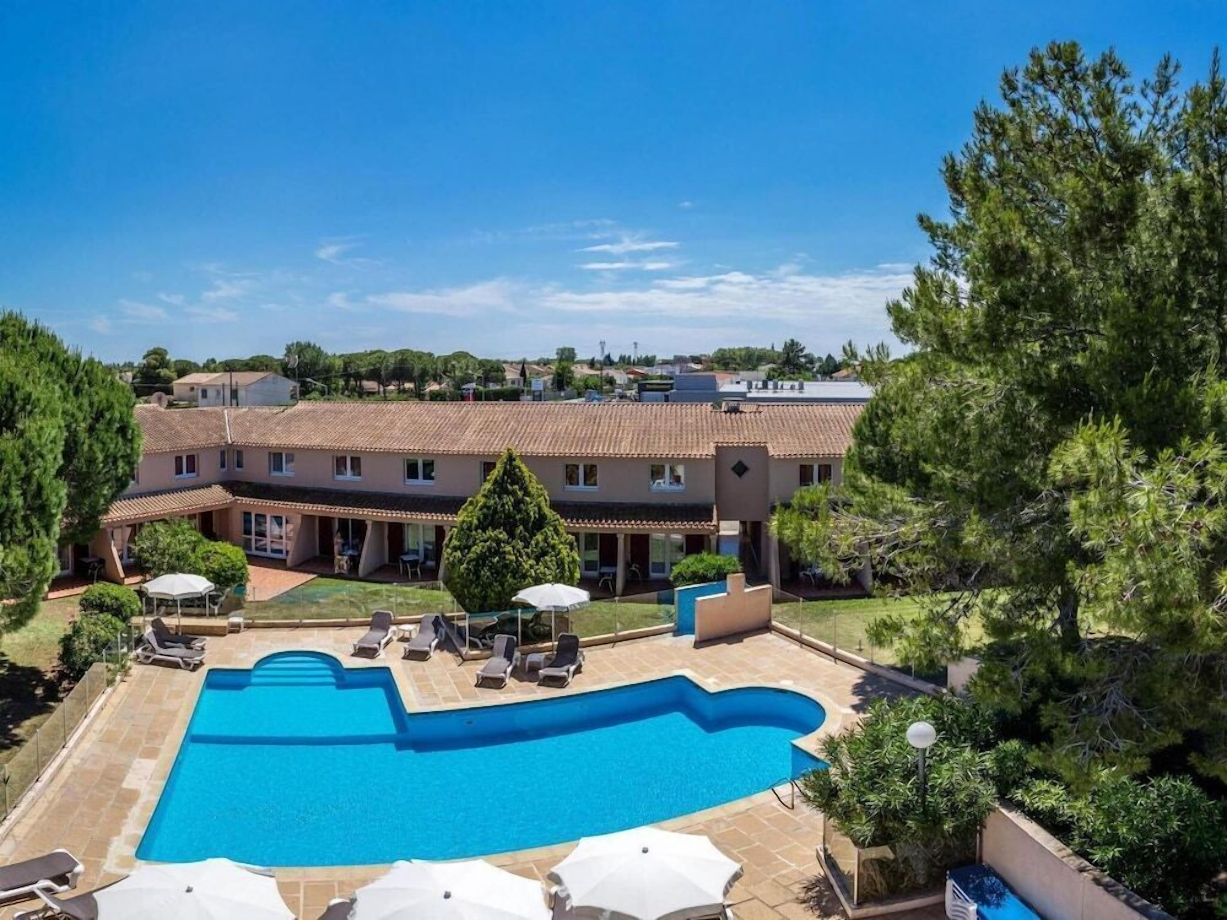 A swimming pool with lounge chairs and umbrellas, surrounded by a building with a tiled roof and a view of the surrounding landscape.