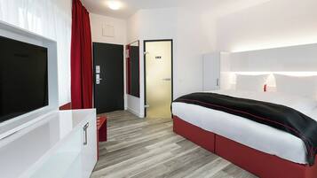 Ein modernes Hotelzimmer mit einem großen Bett, einem Fernseher, einem roten Vorhang und Holzboden.