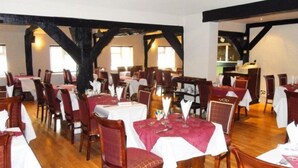 Un restaurant avec des planchers en bois, des tables recouvertes de nappes blanches et des chaises à l’assise rouge.