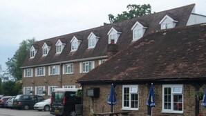 Un pub traditionnel avec une façade en briques, de nombreuses fenêtres et des tables à l’extérieur.