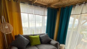A cozy living room with a grey sofa, a woven floor lamp, and a view of the outdoors through sheer curtains.
