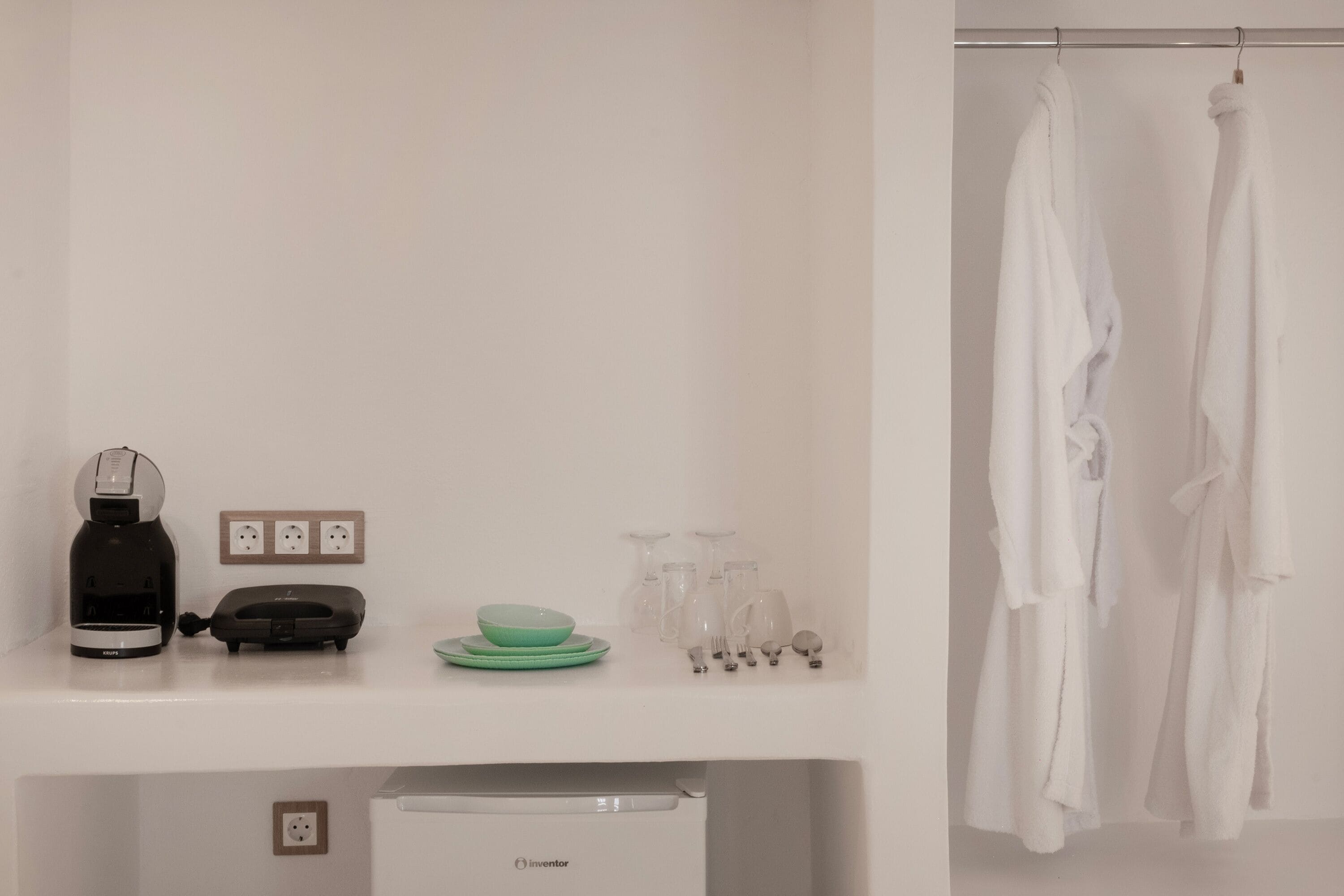 A clean, modern bathroom with a white sink, a black coffee maker, a green bowl, and a white robe hanging on a rack.