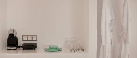 A clean, modern bathroom with a white sink, a black coffee maker, a green bowl, and a white robe hanging on a rack.