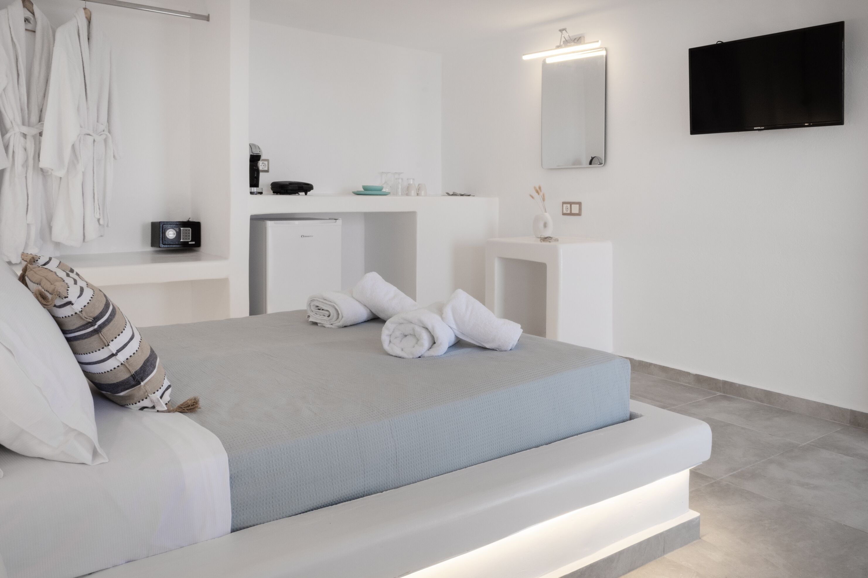 A modern bedroom with a bed, a desk, a mirror, and a TV.