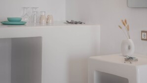 Une pièce au décor minimaliste, avec une table blanche sur laquelle sont disposés un bol turquoise, des verres transparents et une tasse beige.