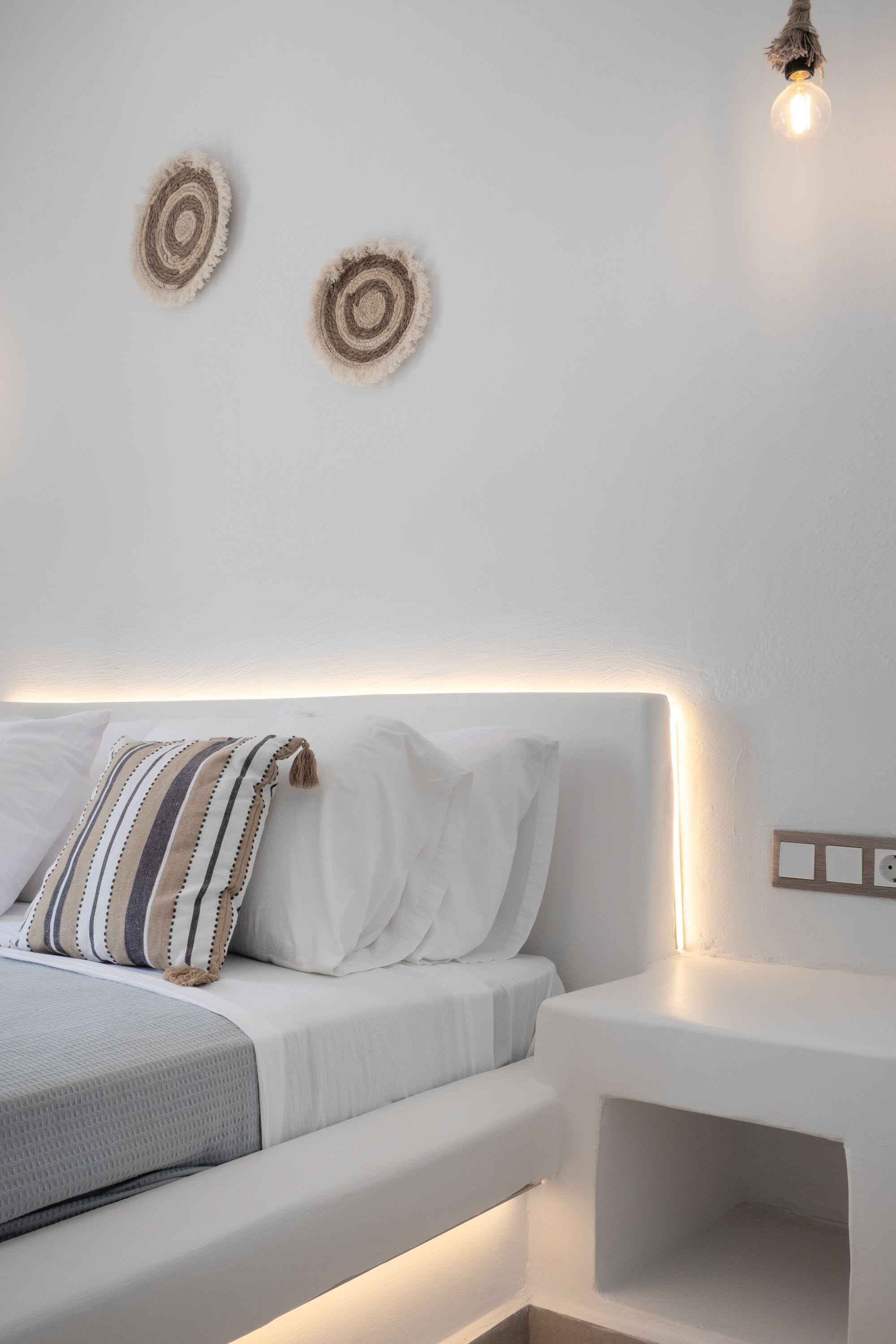 A modern bedroom with a white bed, striped pillow, and a bedside table with a light.