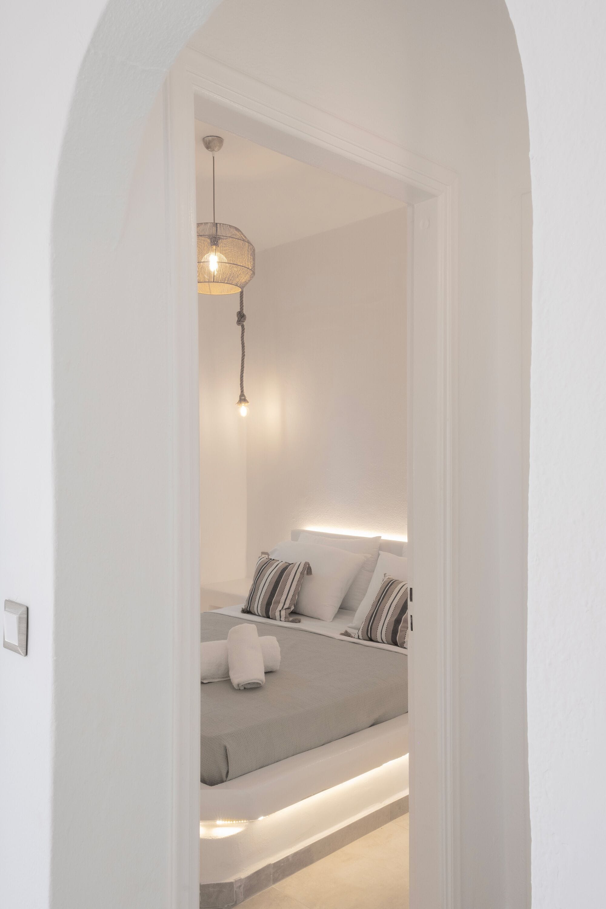 A bedroom with a bed, bedside tables, a hanging light fixture, and a door frame.