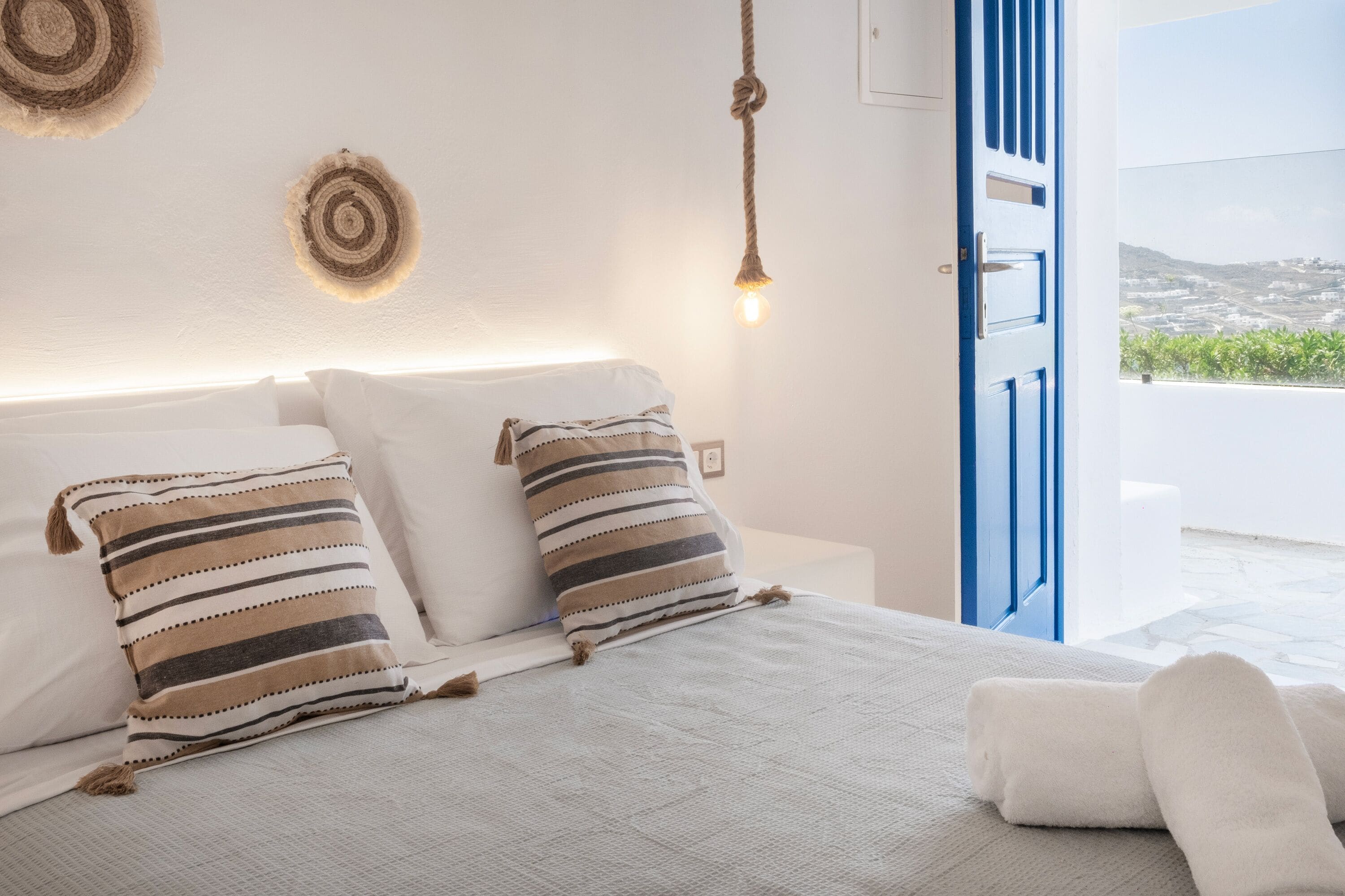 Un dormitorio con cama, almohadas, una lámpara colgante y vistas al exterior.