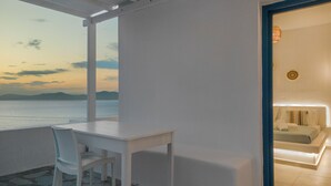 Une pièce avec une table et des chaises blanches, une vue sur la mer et une porte-fenêtre donnant sur un espace aménagé en chambre.