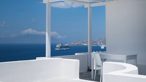 Un espace extérieur aménagé avec des sièges blancs, offrant une vue sur la mer et un navire de croisière.